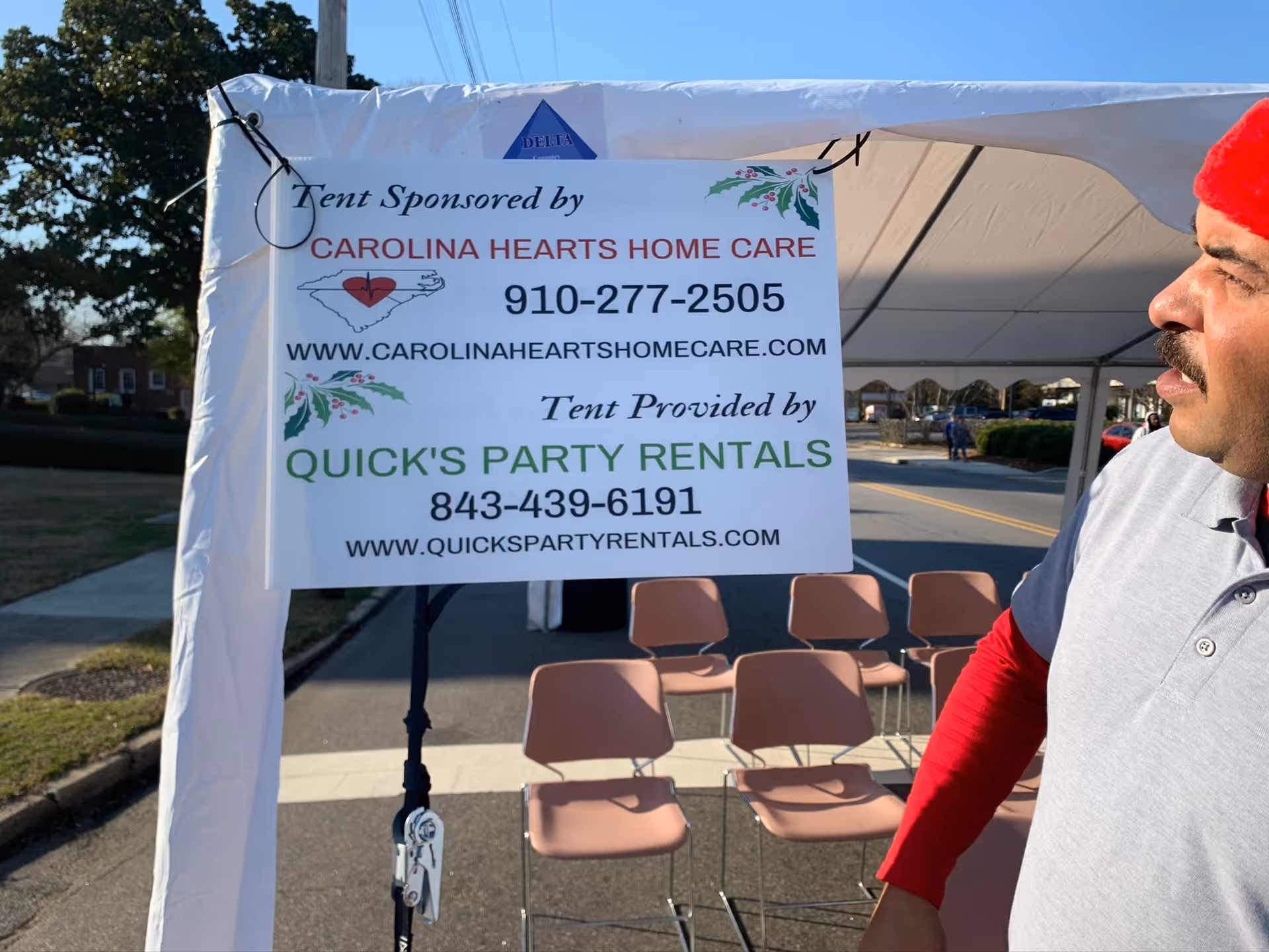 Outdoor tent with a Carolina Hearts Home Care sign and empty chairs.
