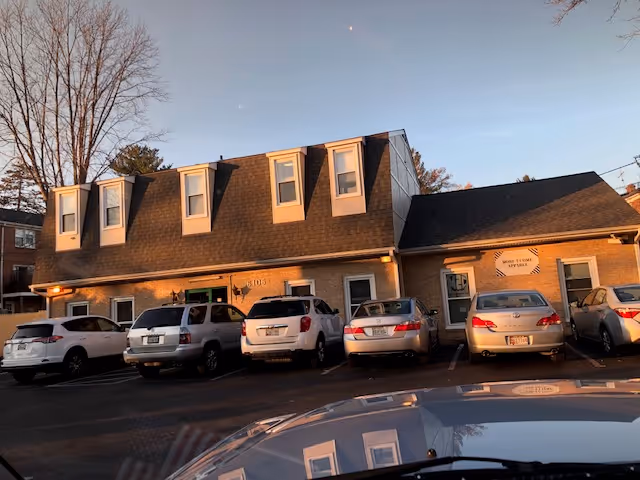 Exterior view of a brick senior living building with dormer windows and parked cars.