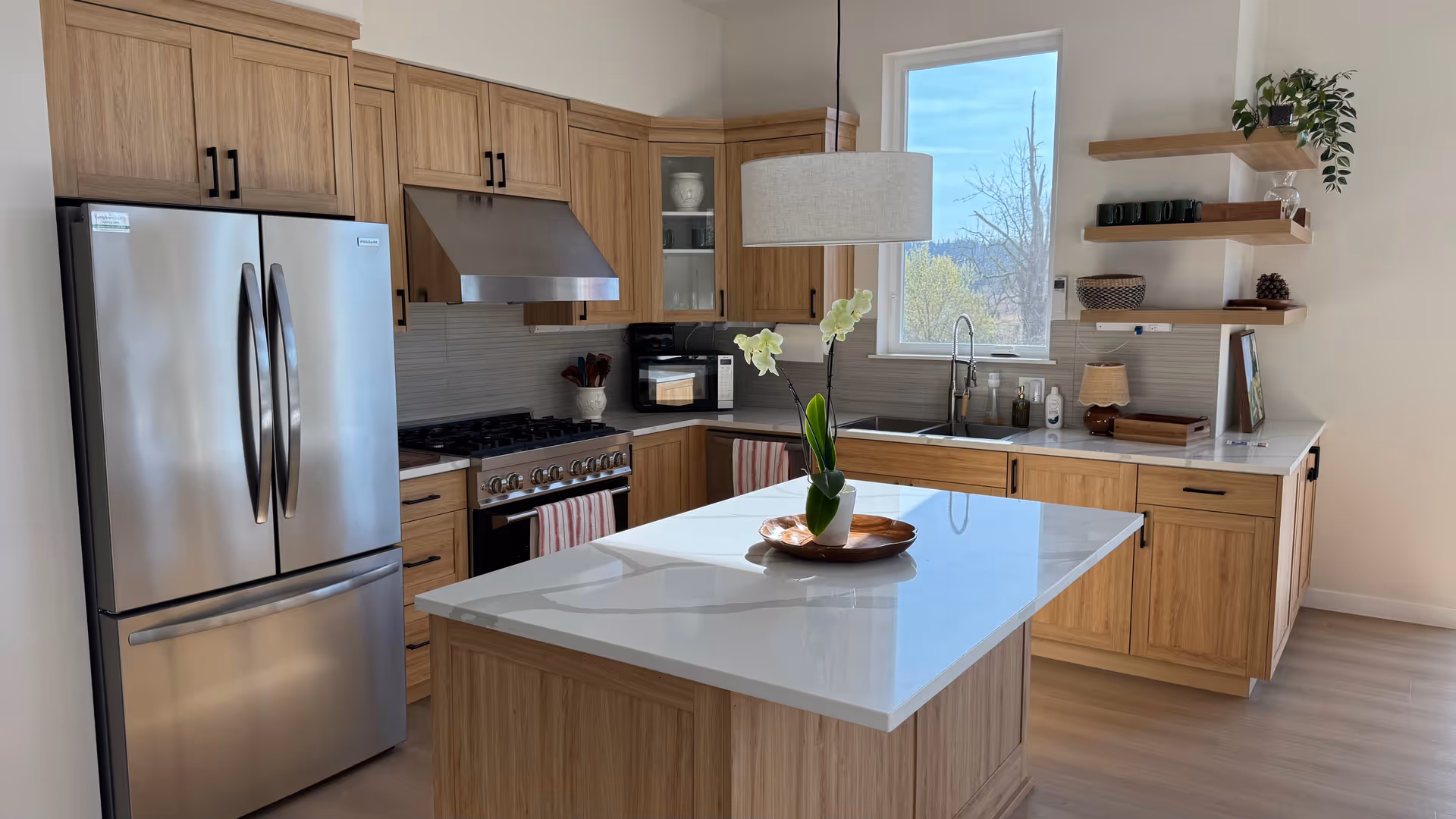 Bright modern kitchen with wooden cabinets, stainless appliances, island, and open shelving.