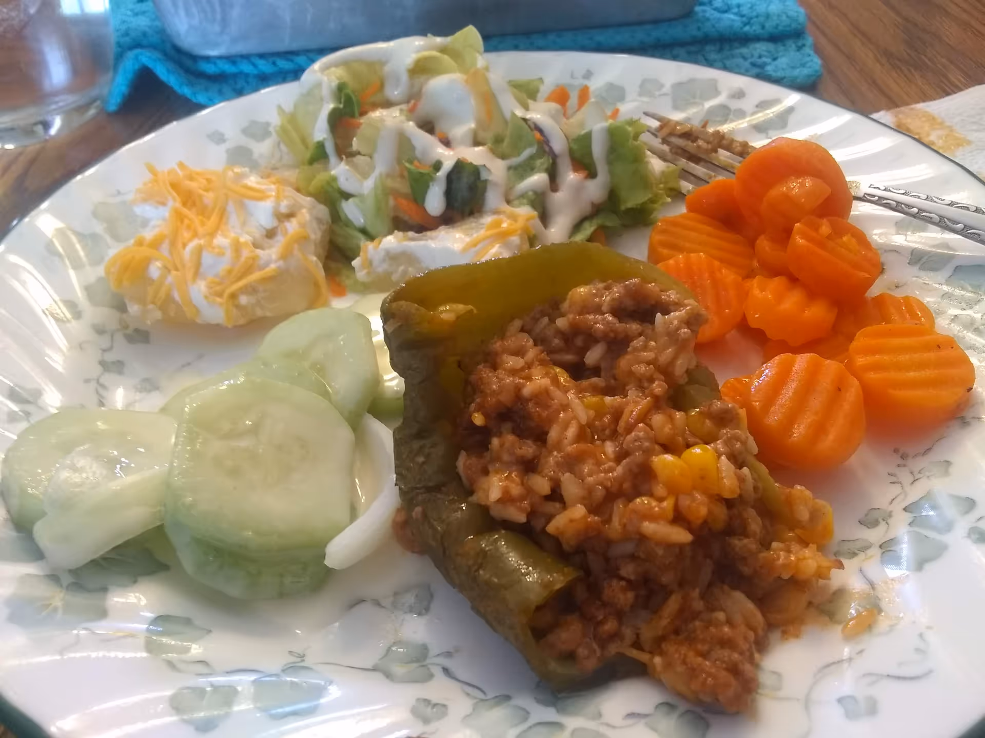 Plate of mixed vegetables, stuffed pepper, salad, cucumbers, and crinkle-cut carrot coins on a table.