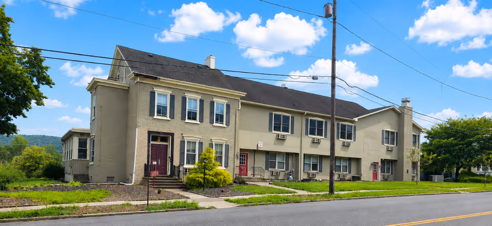 A two-story beige memory care building sits along a quiet street with green lawns.