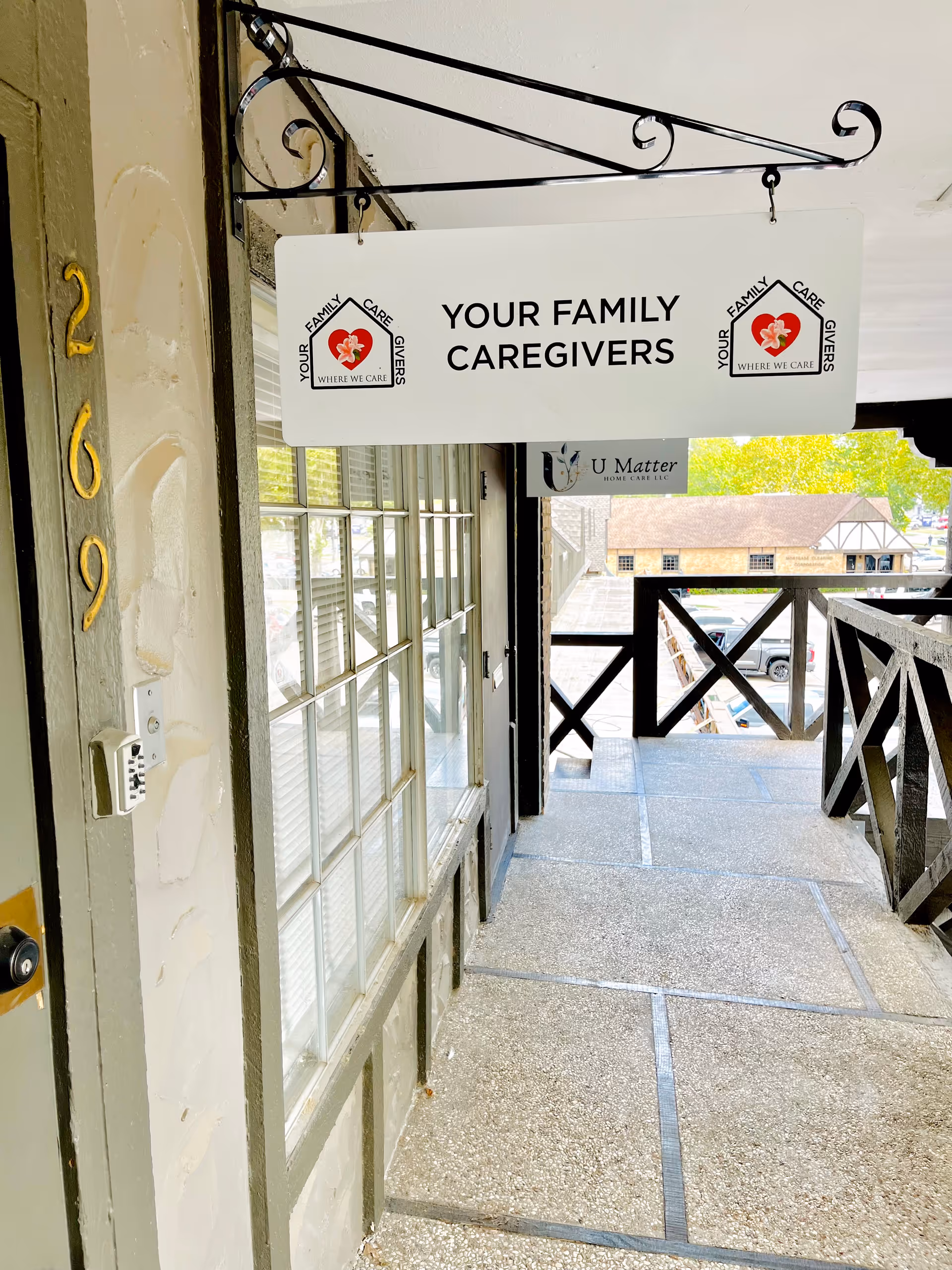 Exterior building entrance with hanging Your Family Caregivers sign and balcony railing.
