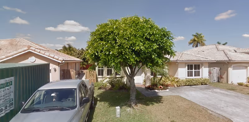 Single-story ranch-style house front with a driveway, a parked silver pickup truck, and a small tree in the front yard.