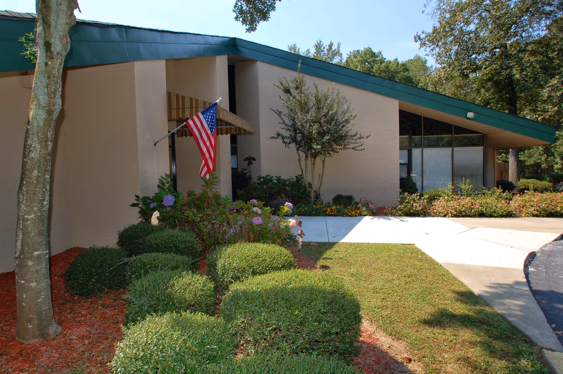 Country Gardens Dunwoody facility exterior with American flag, lush shrubs, and a curved sidewalk.