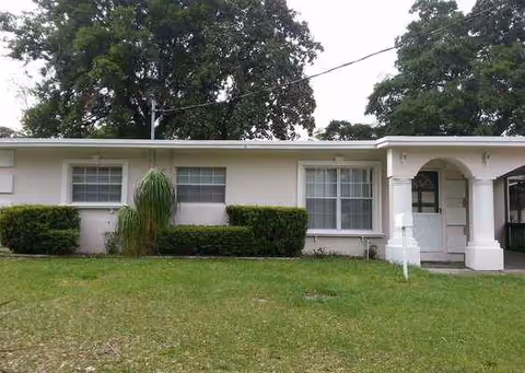 Single-story white care home with front entrance, archway, windows, trimmed hedges, and lawn.