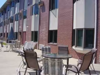 Outdoor patio with round table and chairs in front of brick apartment building.