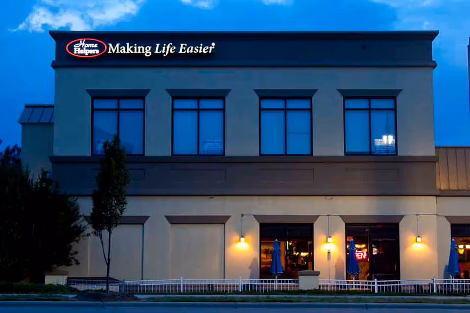 Two-story facility with Home Helpers sign, large windows, and outdoor seating at front entrance.
