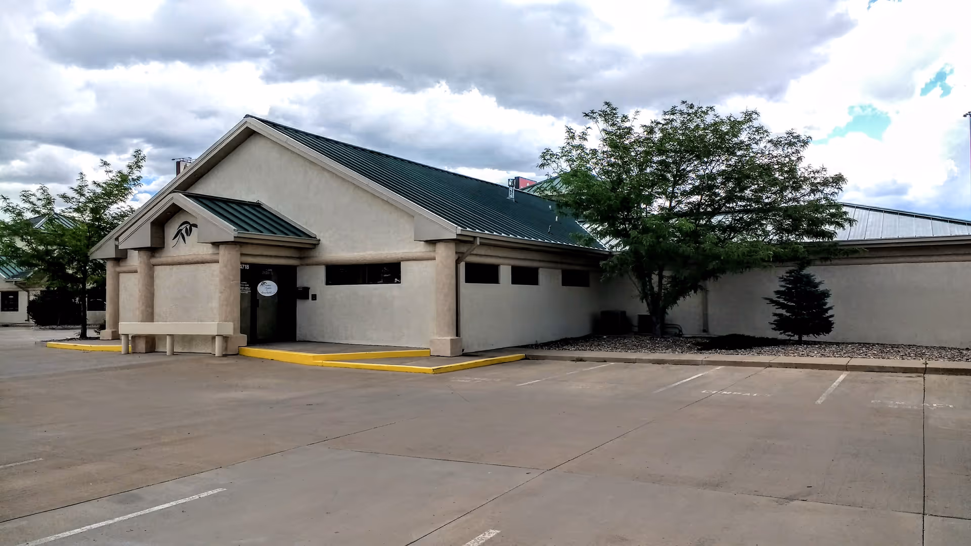 Front exterior view of a single-story facility with a driveway and entrance under a green roof.
