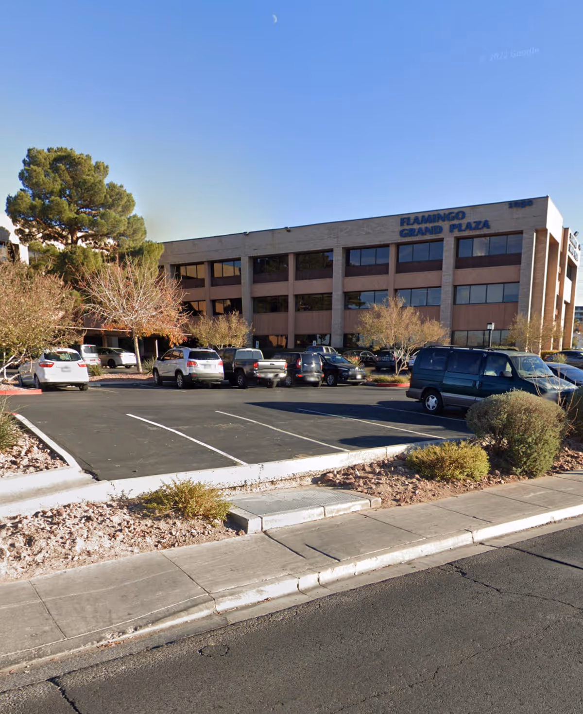 Exterior view of Flamingo Grand Plaza with parked cars and desert landscaping.