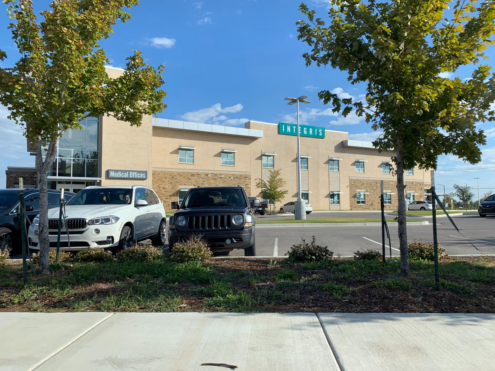 Exterior view of INTEGRIS Health Community Hospital Council Crossing with parked cars and trees.