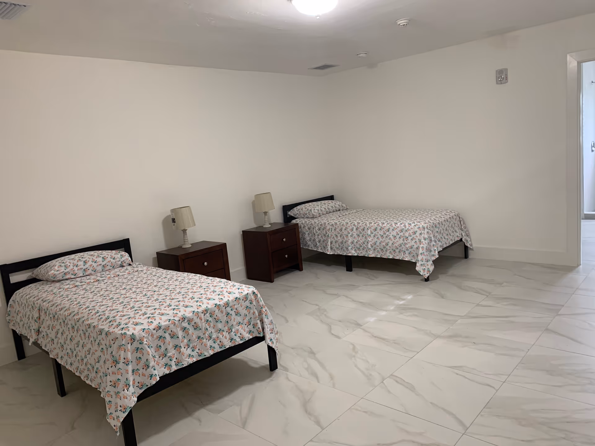 Two single beds with floral bedding and matching nightstands in a spacious, minimal bedroom.