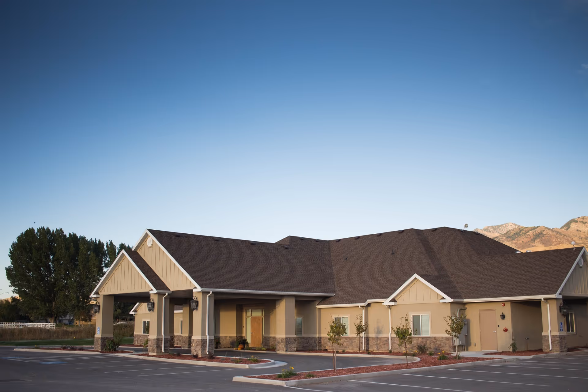 Single-story senior living center with brown roof and beige facade, parking lot in front.