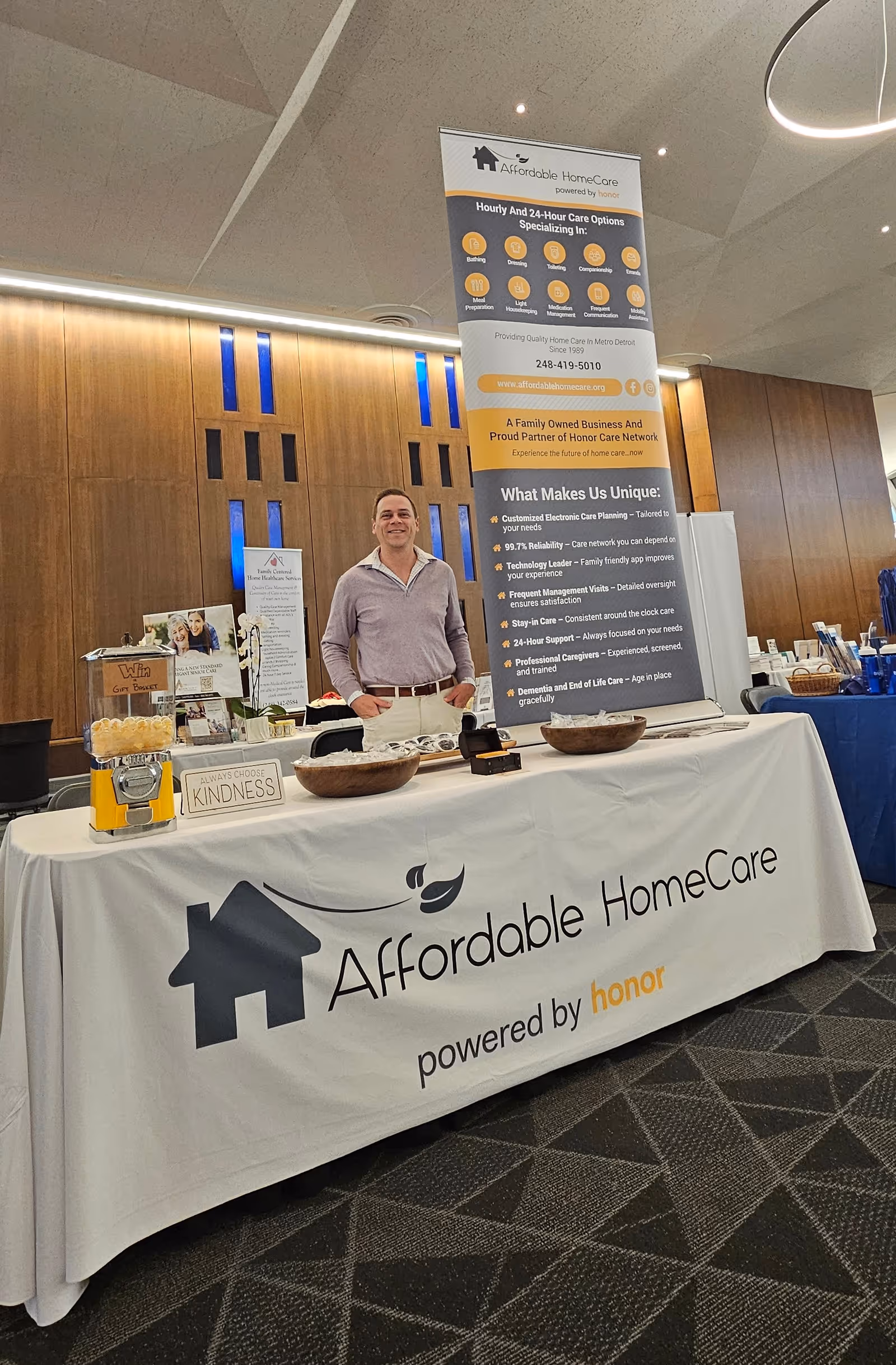Man stands beside a booth promoting Affordable HomeCare at an indoor expo.