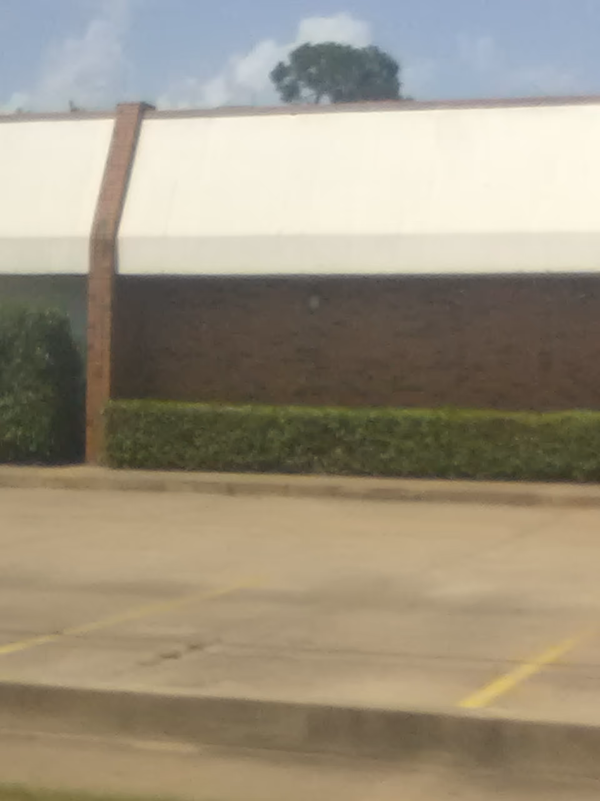 Exterior view of a brown-brick building with a white upper facade and trimmed hedges.