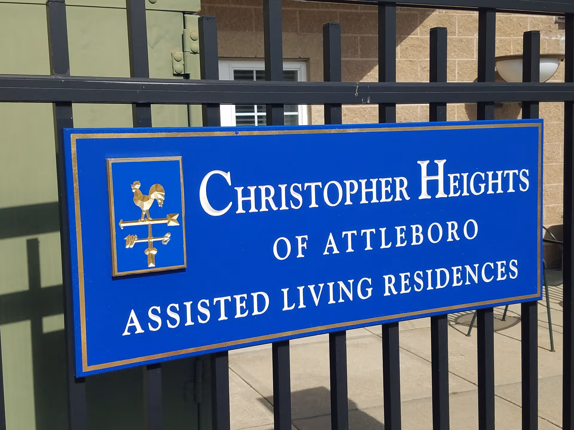 Blue sign reading Christopher Heights of Attleboro Assisted Living Residences behind a black fence