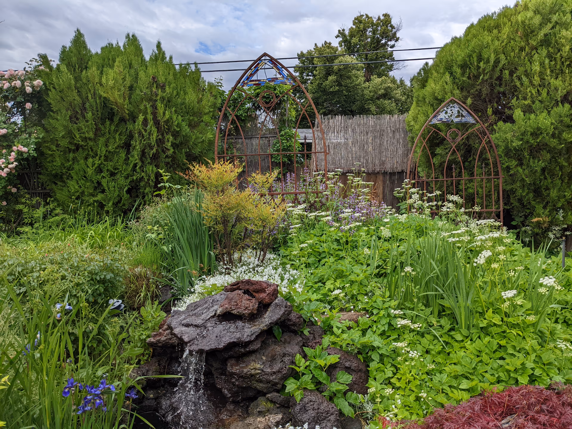Lush garden with flowering plants, rocks, and decorative metal arch structures.