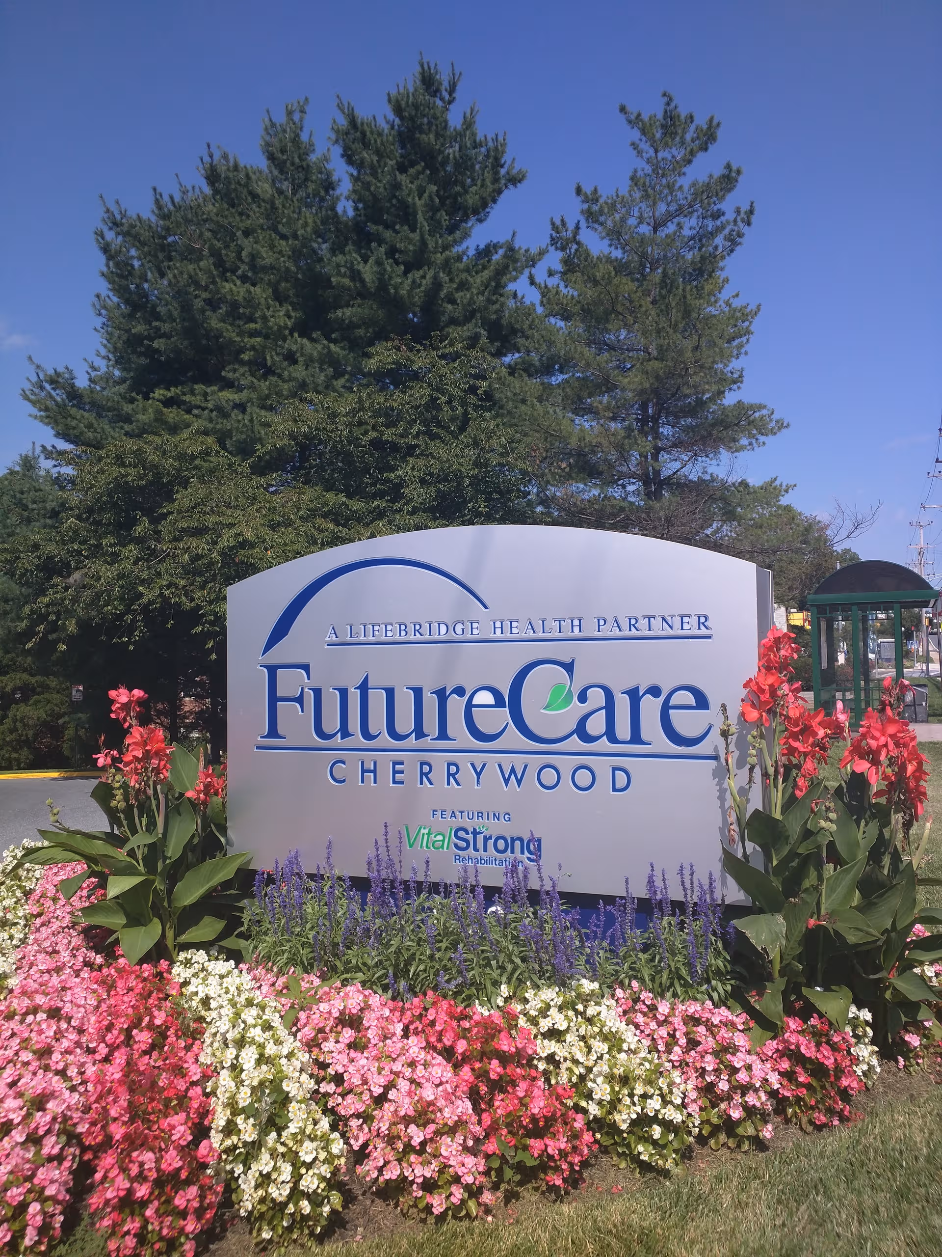 Outdoor entrance sign reads FutureCare Cherrywood amid colorful flower beds and trees.