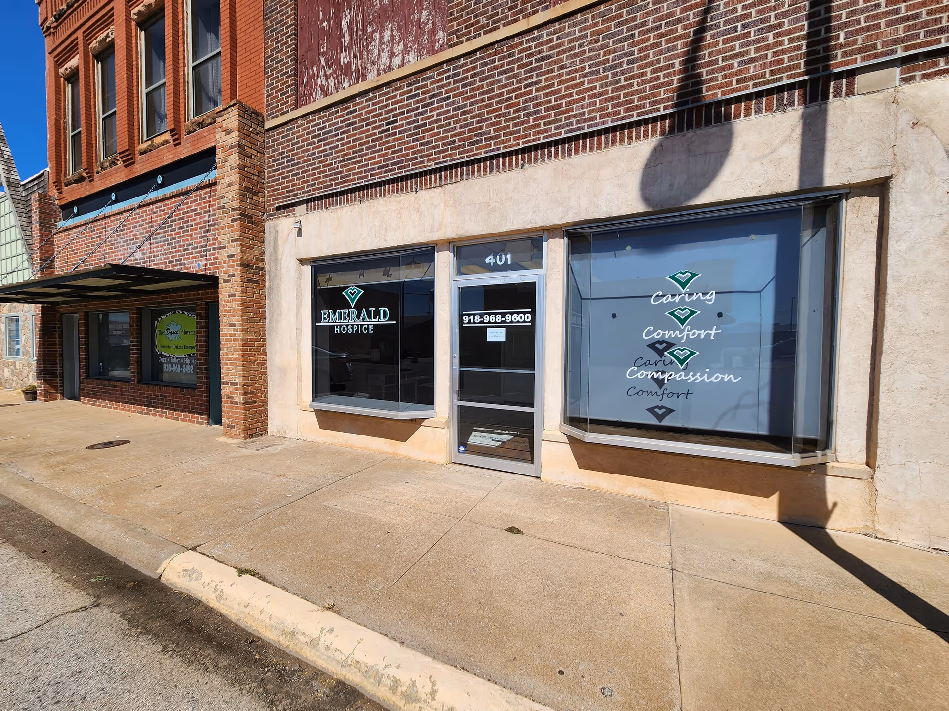 Exterior view of a brick building with Emerald Hospice storefront and large display windows.