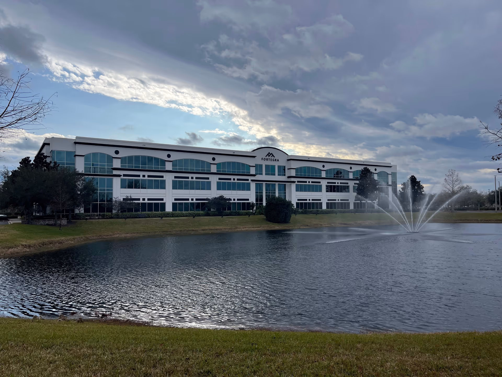 Modern multi-story care facility exterior beside a pond with a fountain.