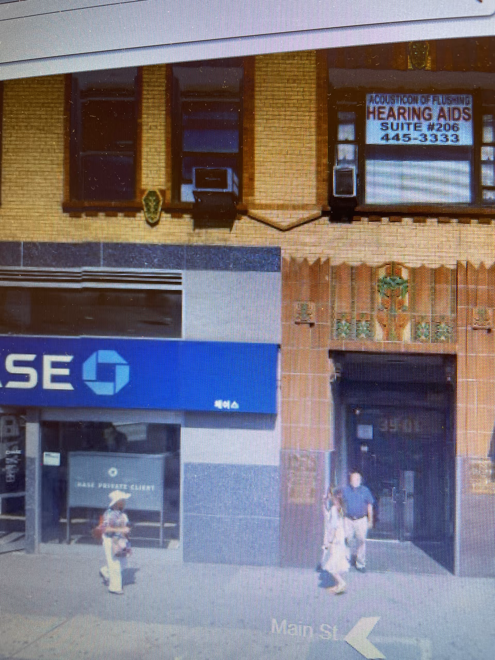 City street storefront with hearing aids sign and pedestrians near a doorway.