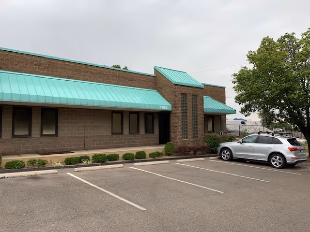Brick senior care building with turquoise awnings and a parking lot in front.