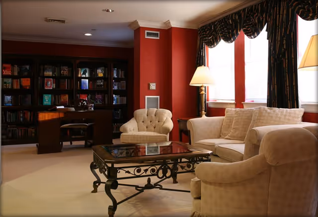 Luxurious living room with cream furniture, glass coffee table, and bookshelves along red-walled interior.