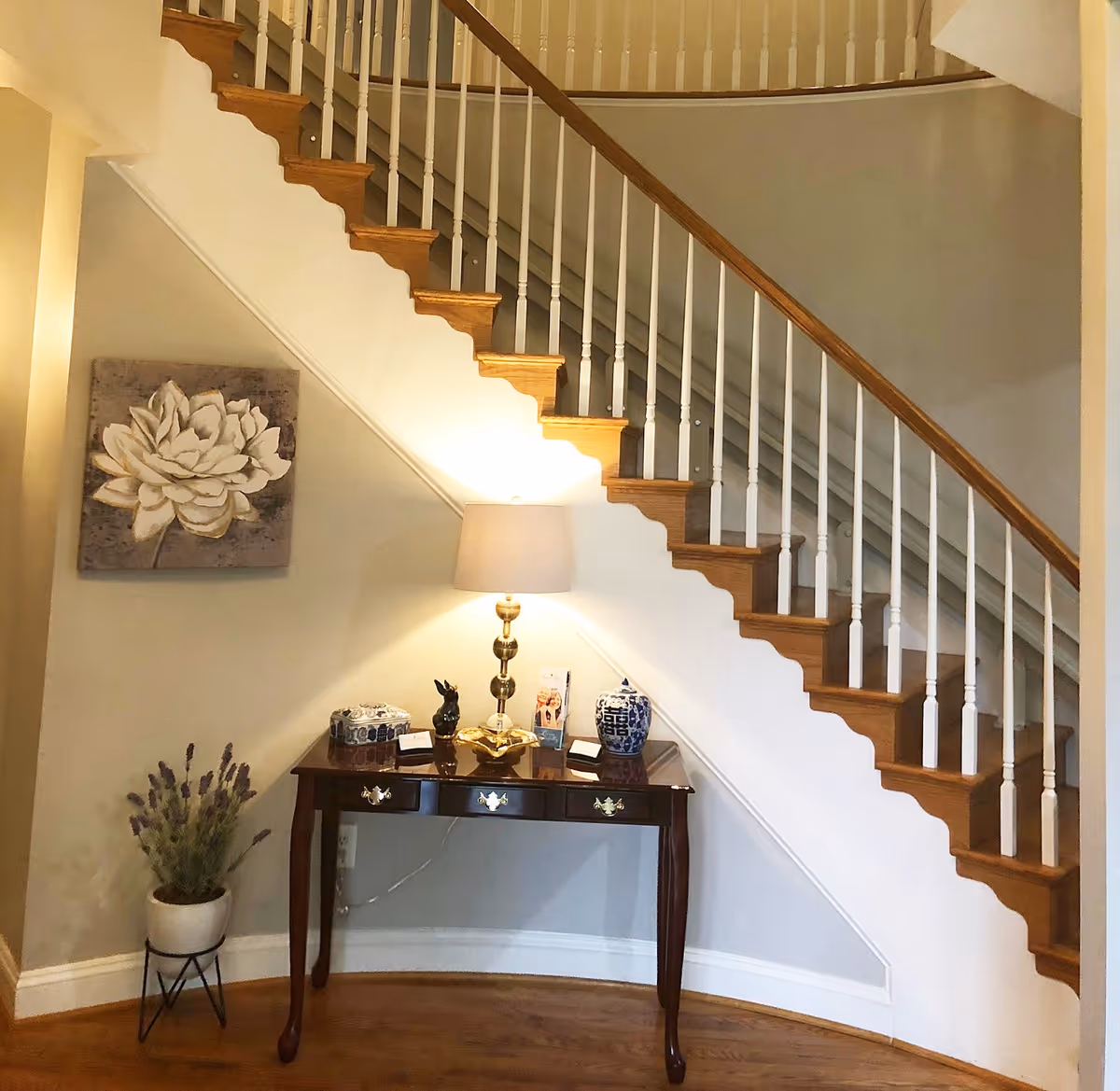 Entryway with curved staircase, console table, lamp, and decorative plants.
