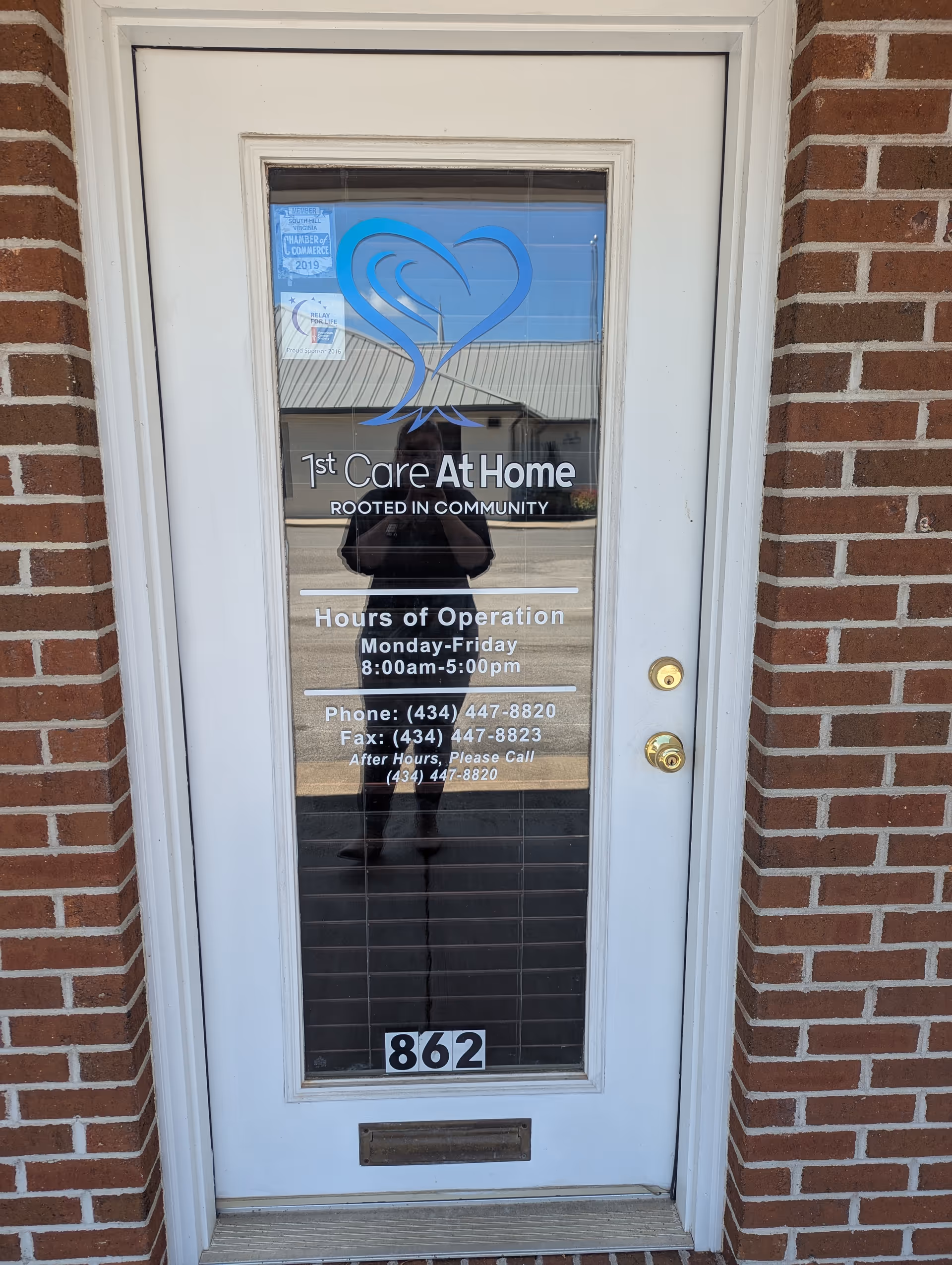 Glass door displaying the 1st Care At Home logo and hours against a brick exterior.