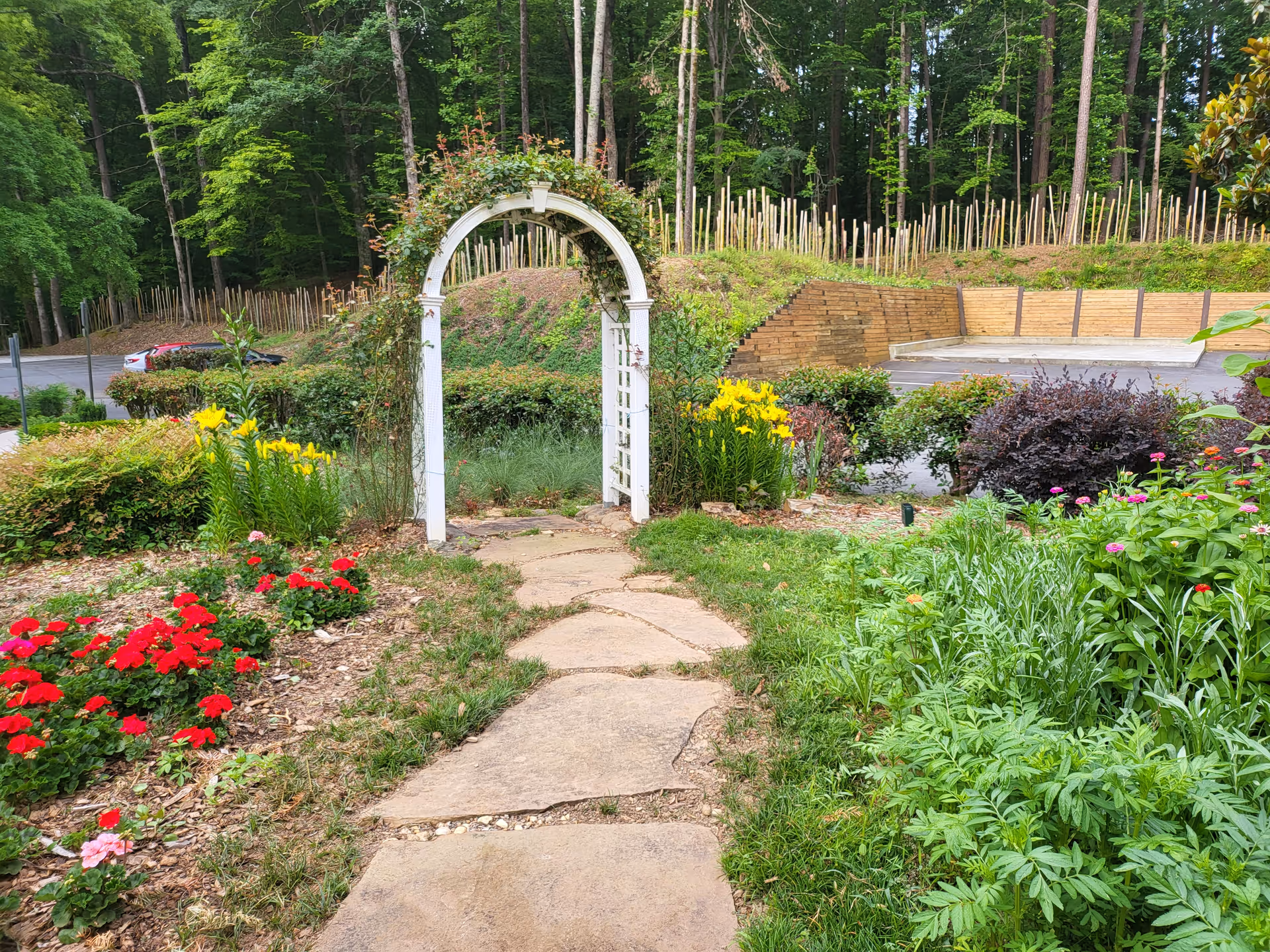Stone path winds through a colorful garden with a white arch.