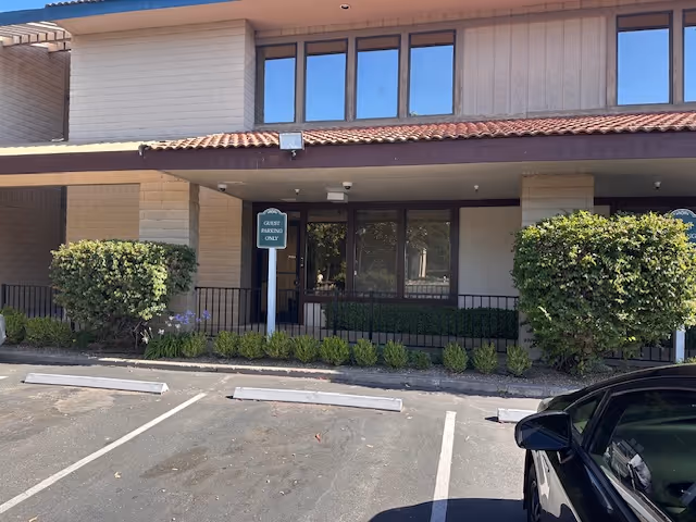 Front exterior of a senior living facility with entrance, parking spaces, and shrubs.