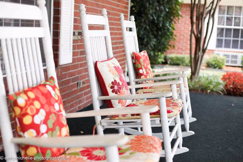 White wooden rocking chairs with colorful floral cushions lined up on a brick porch.