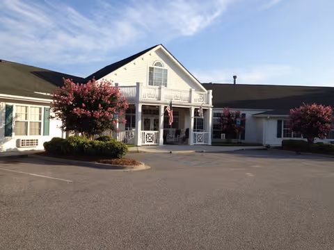 Senior living facility with white siding, central entrance, and pink flowering trees.