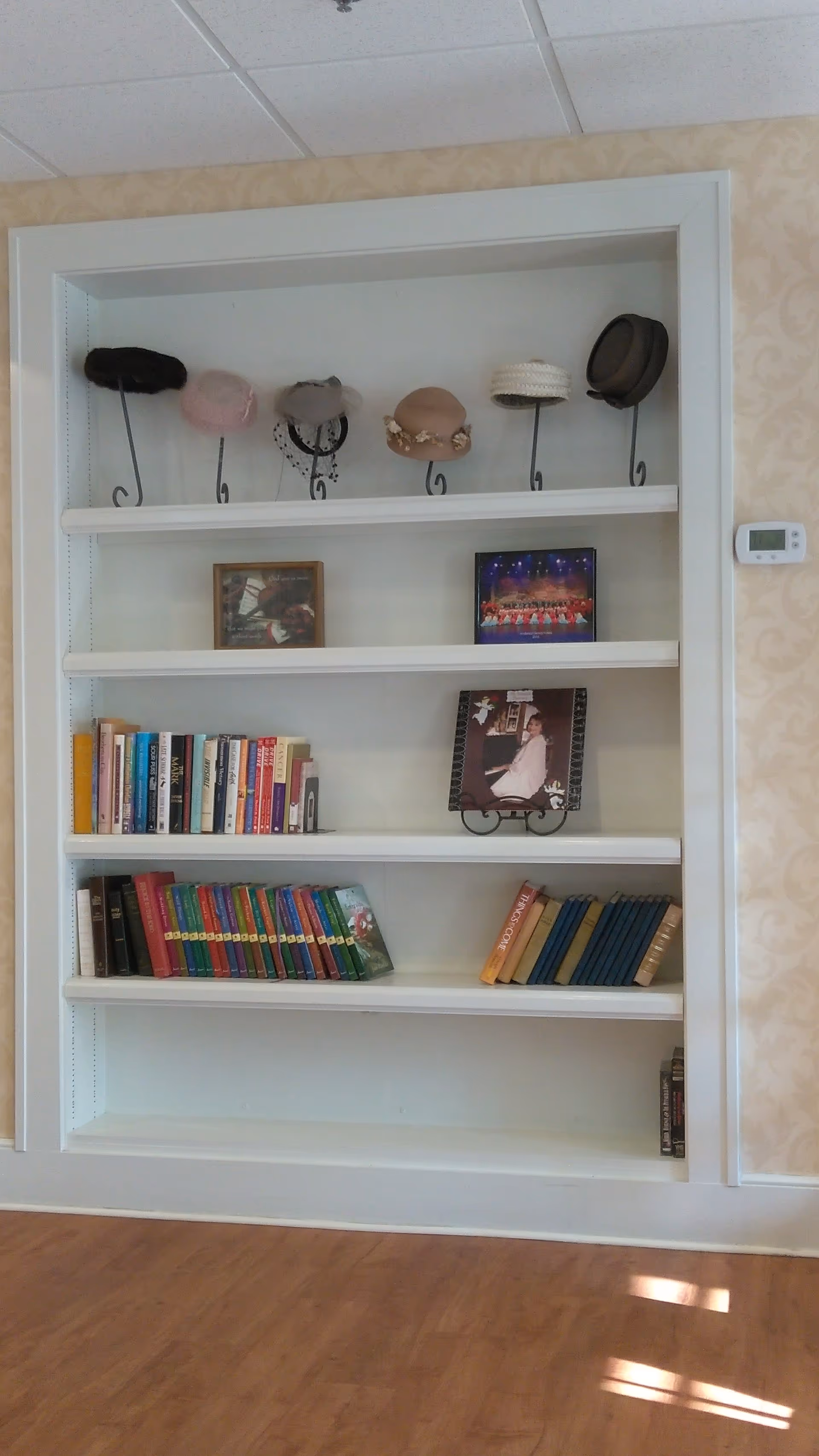 Built-in white bookshelf alcove with hats, photos, and books in a hallway.