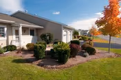 Front exterior of a senior living facility with manicured shrubs and a paved walkway.