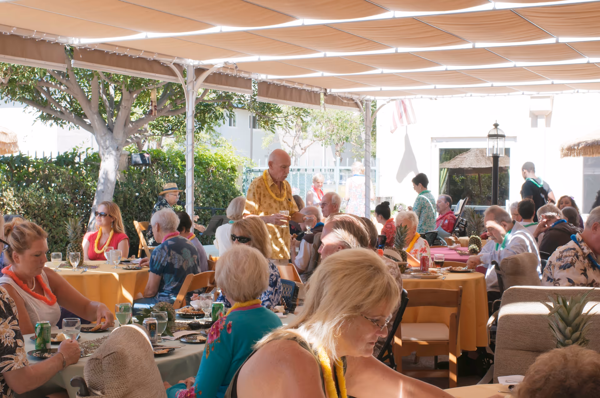 Outdoor covered courtyard where seniors dine at tables under a tan canopy.