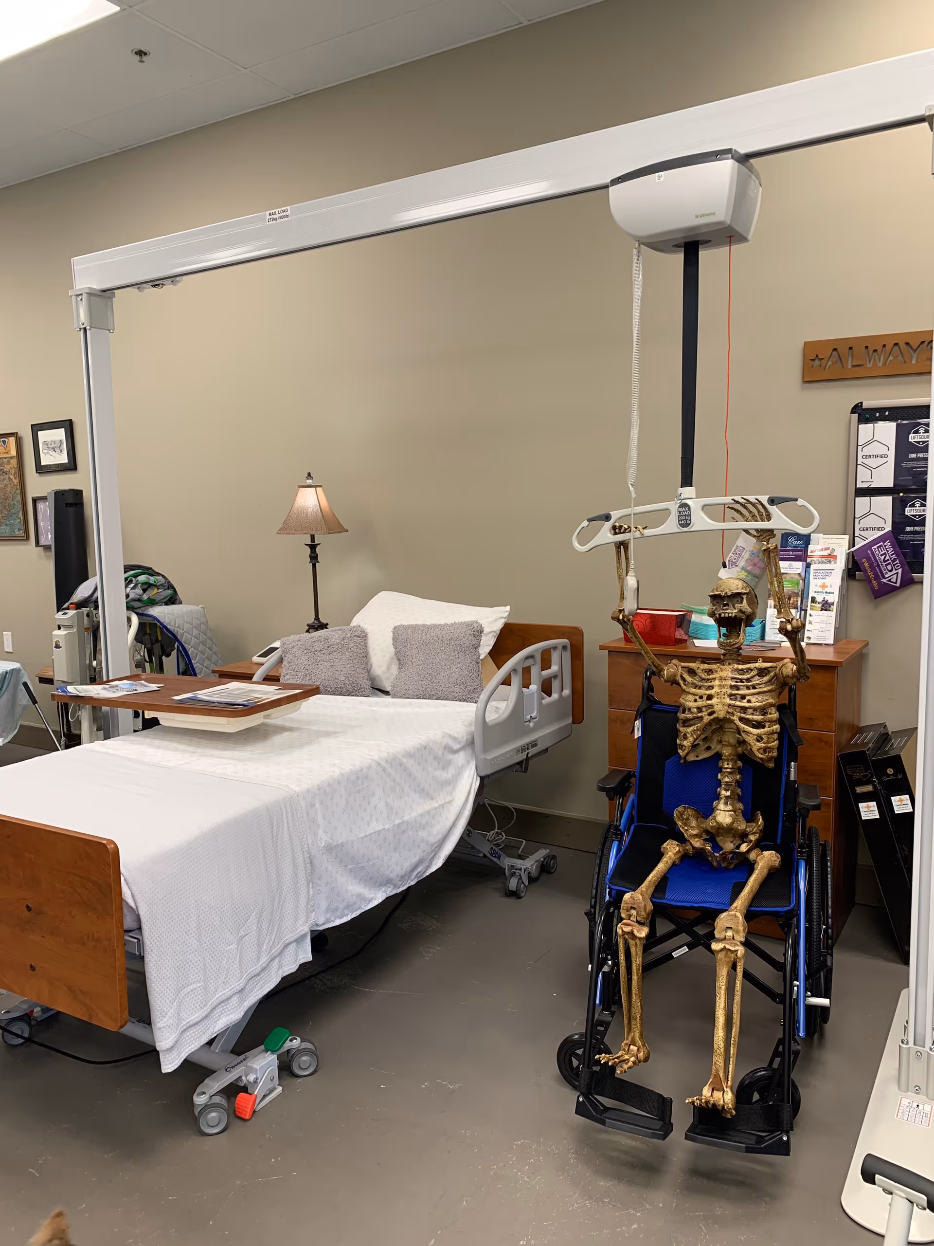 Hospital-style patient room with bed, overhead lift, and skeleton on a wheelchair.