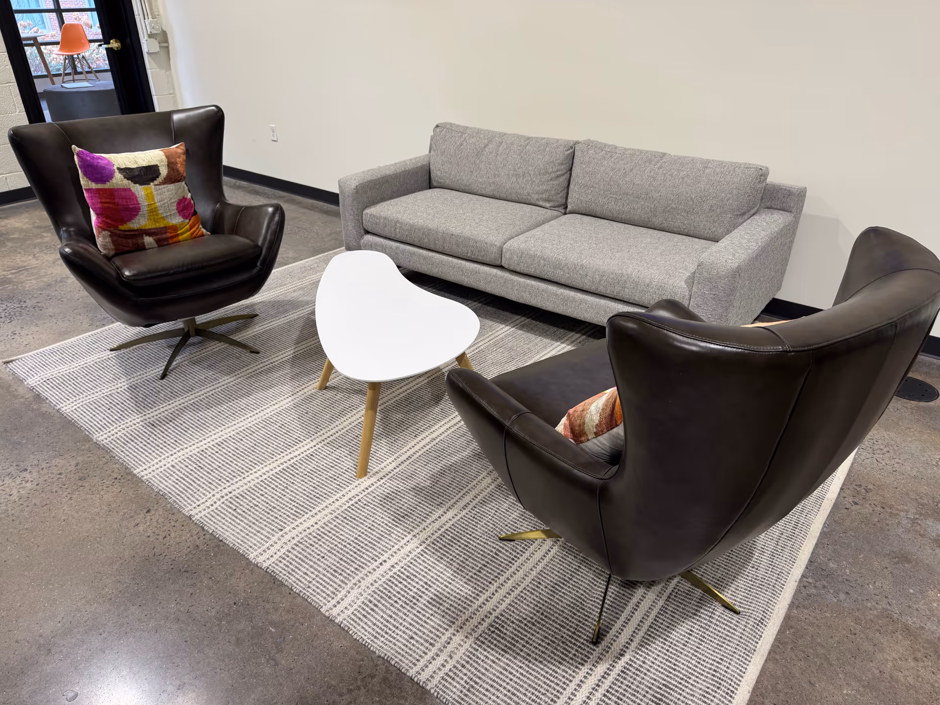 Modern lounge area with gray sofa, black leather chairs, and a heart-shaped white table.