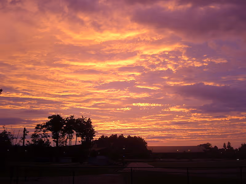 Sunset sky with orange clouds over a dark landscape and silhouetted trees.