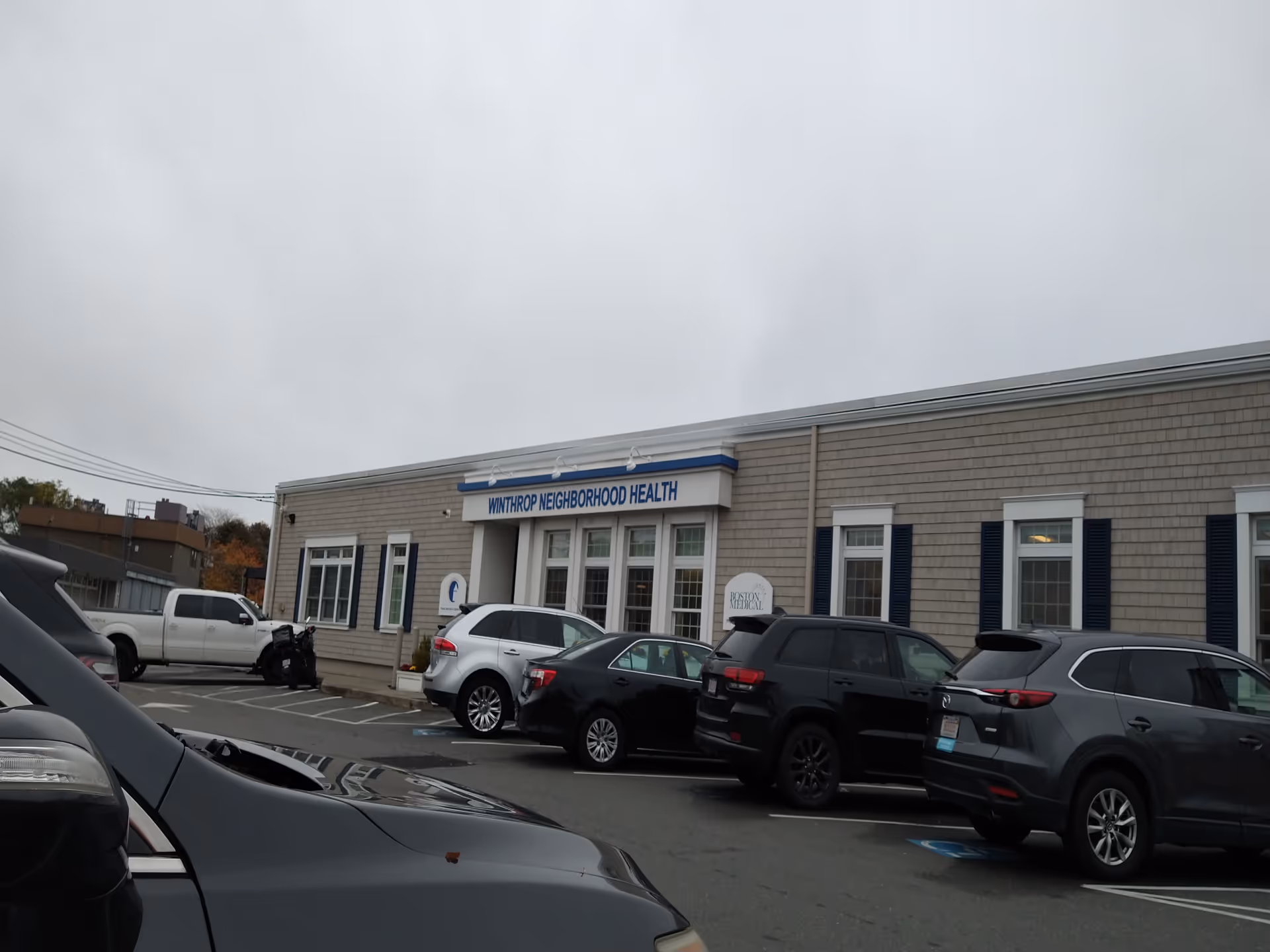 Exterior view of a health clinic building with a sign and parked cars.