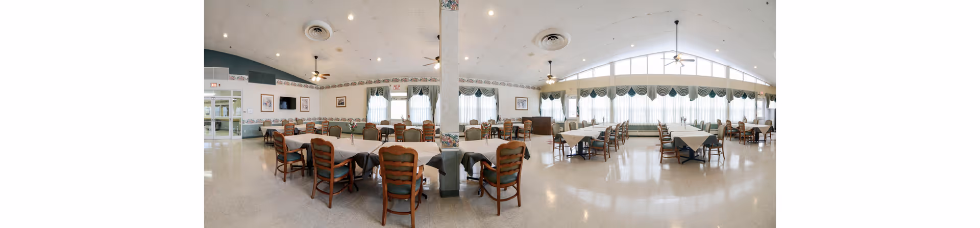 Spacious dining room with multiple tables and chairs, large windows with valances, and a high vaulted ceiling.