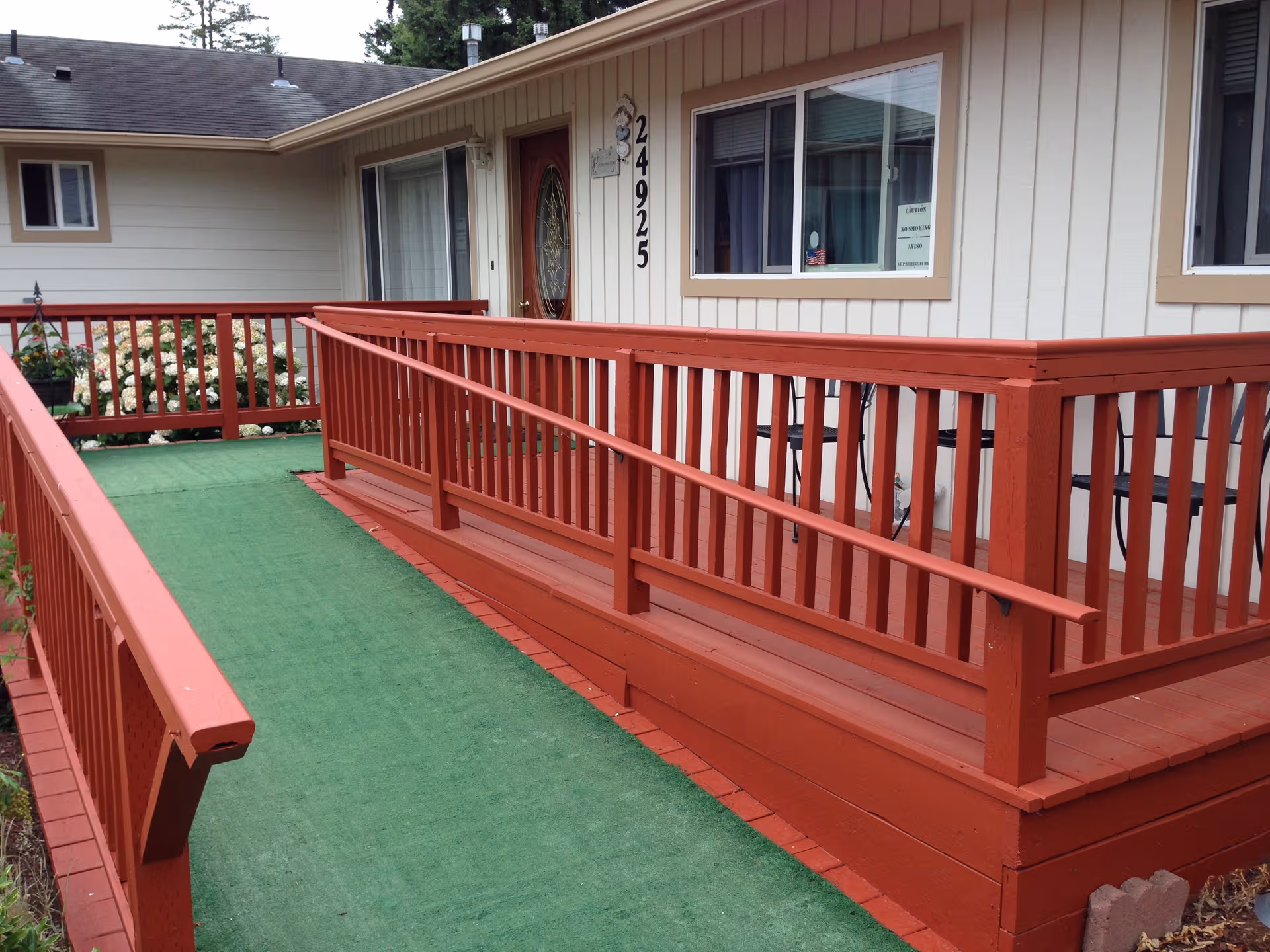 Red wooden ramp with railing leads to the entrance of a senior care facility.