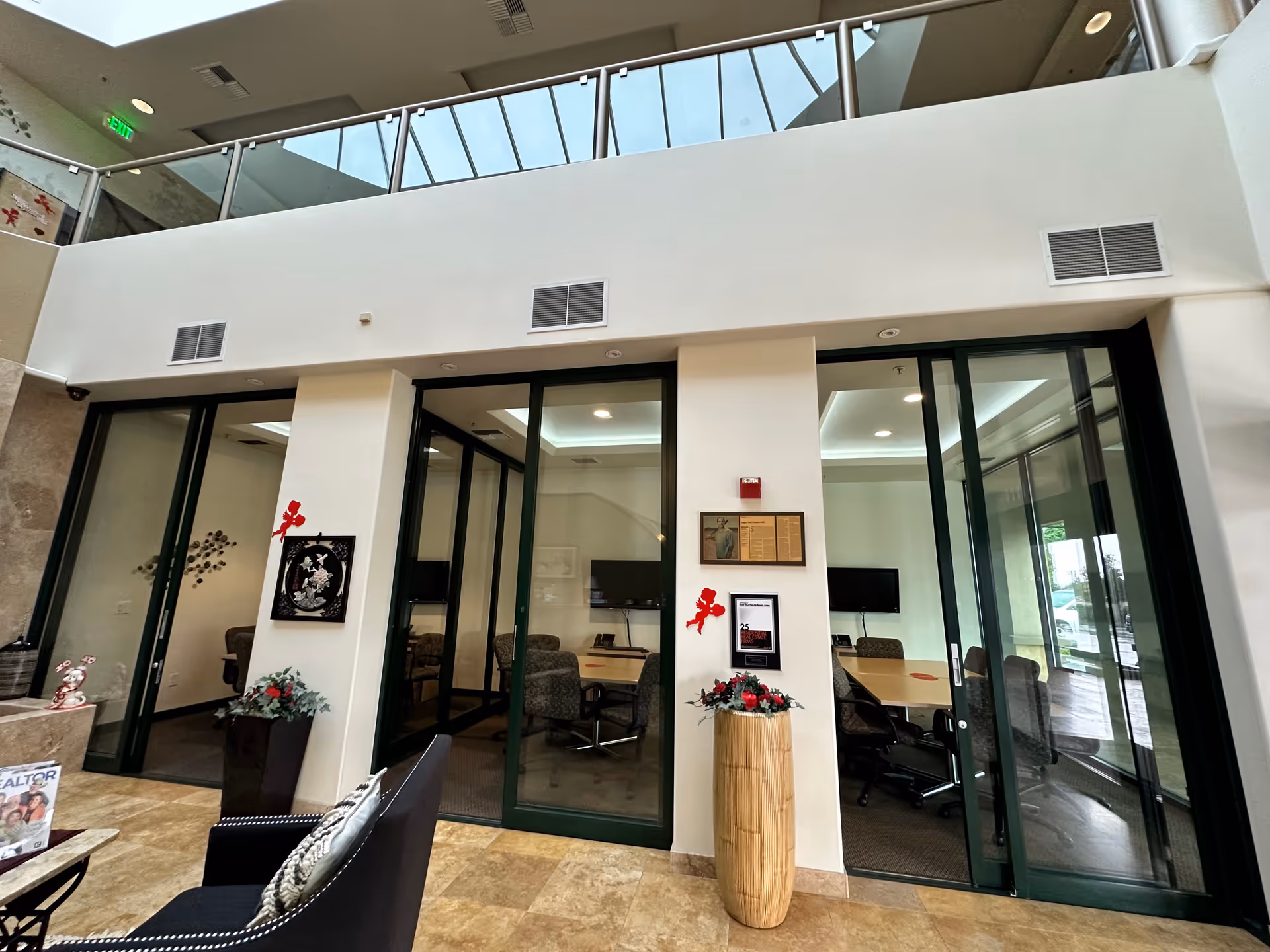 Modern interior lobby with glass-walled meeting rooms, chairs, and decorative plants.