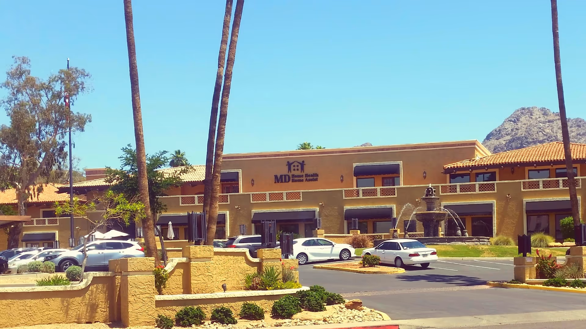 Front of a tan MD Home Health building with a fountain and palm trees