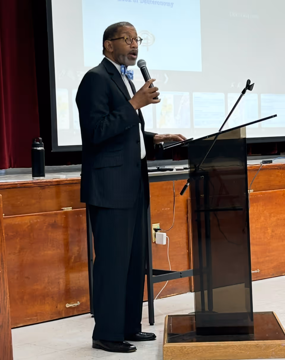 A speaker in a suit addresses an audience from a podium.