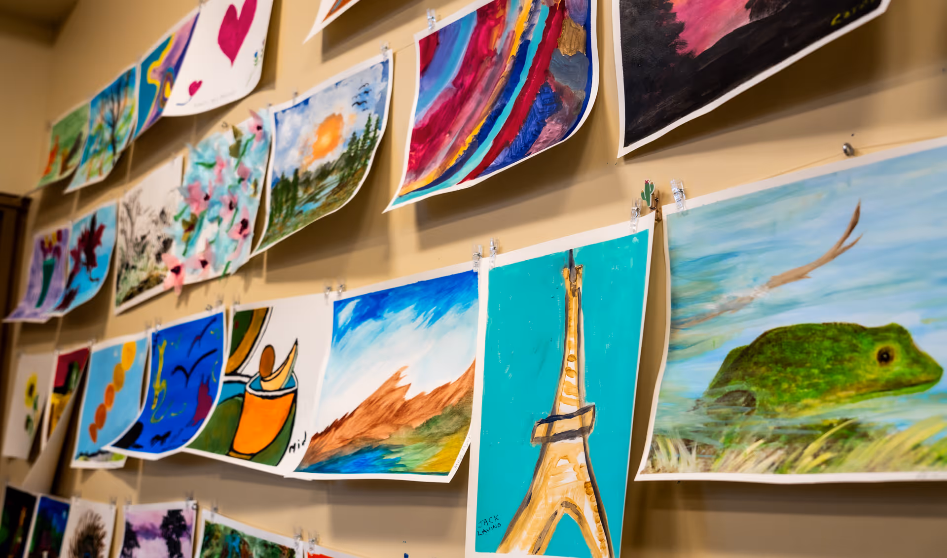 Interior wall displaying colorful paintings clipped along a string in a seniors' activity area.