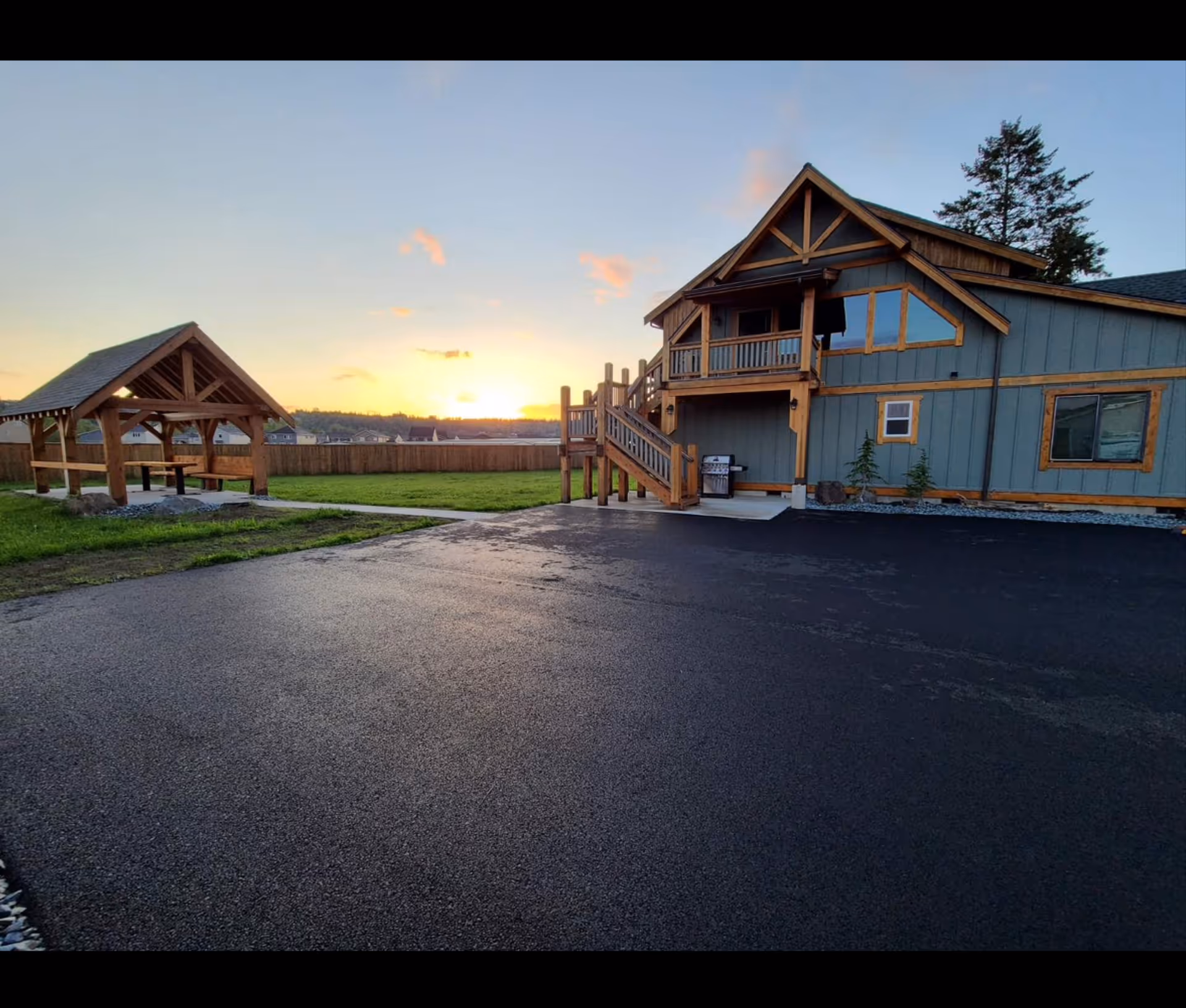 Sunset over a wooden two-story facility with an outdoor pavilion and paved driveway.