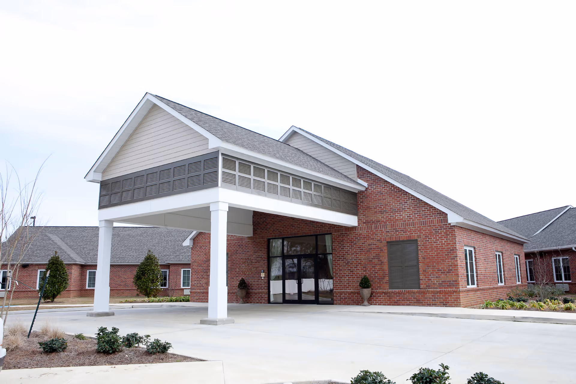 Front entrance of a single-story brick senior living facility with a covered porte-cochère and glass double doors.
