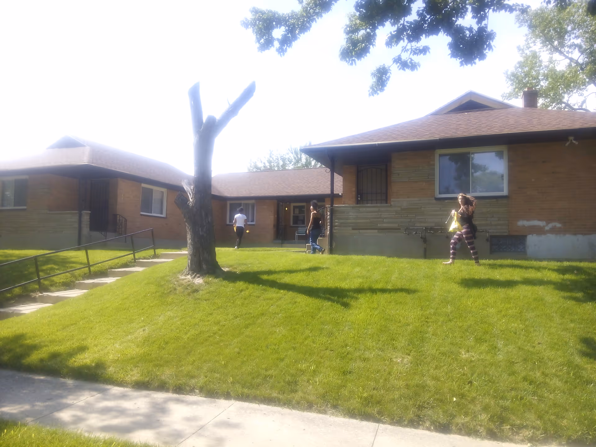 Exterior view of a brick building with a grassy hill and three people walking outside.