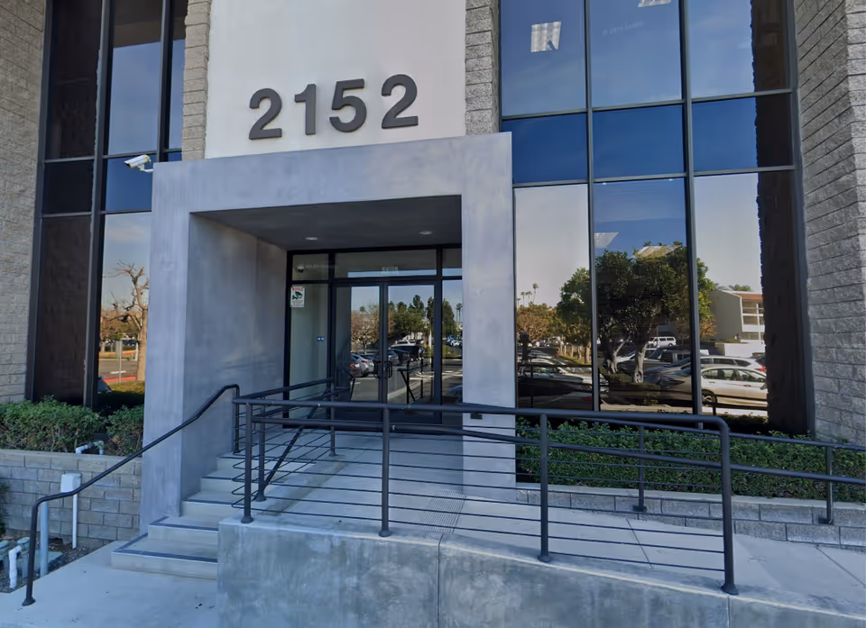 Exterior view of a modern building entrance with concrete ramp and glass doors.