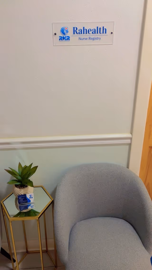 Interior hallway seating area with Rahealth Nurse Registry sign, gray chair, and plant.